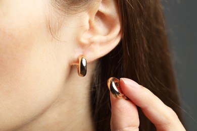 Photo of Woman wearing beautiful golden earring on grey background, closeup