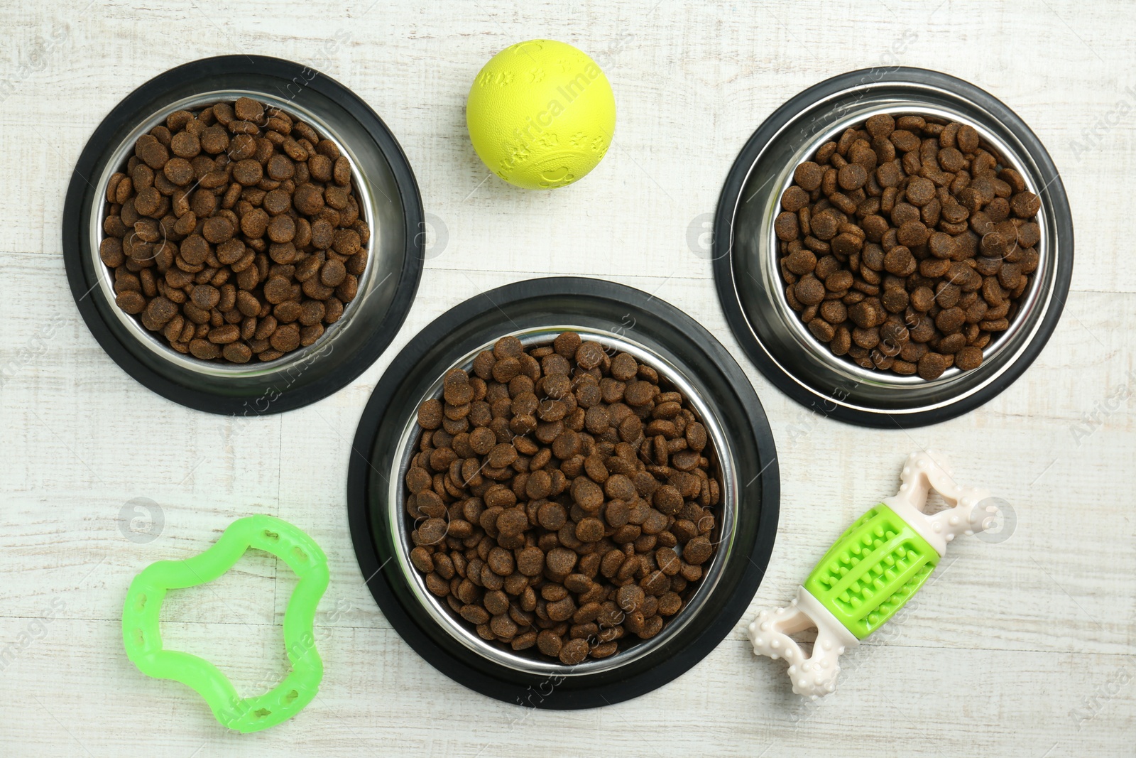 Photo of Dry pet food in feeding bowls and toys on floor, flat lay