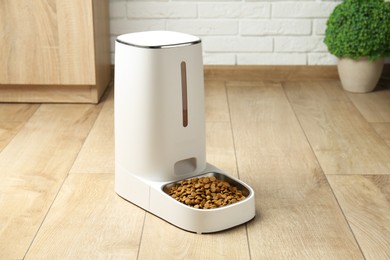 Photo of Dry pet food in automatic feeder on floor indoors