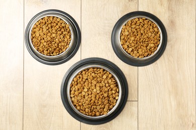 Photo of Dry pet food in feeding bowls on wooden floor, flat lay