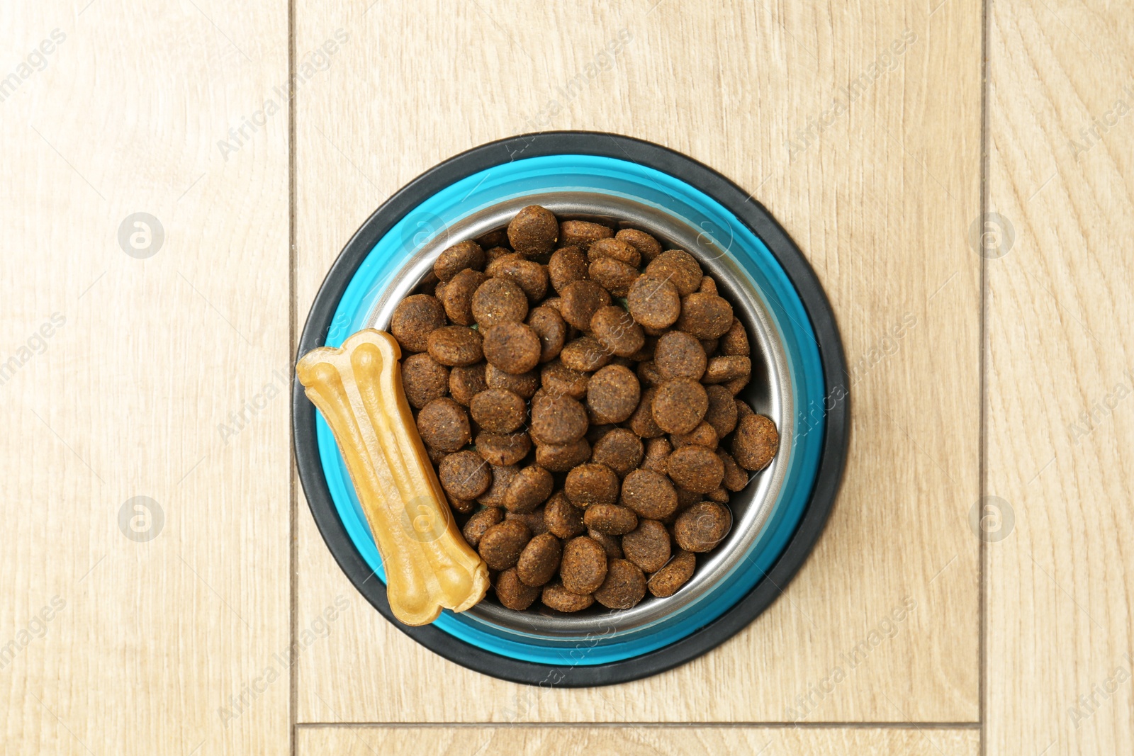 Photo of Dry pet food in feeding bowl and chew bone on wooden floor, top view