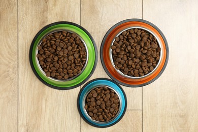 Photo of Dry pet food in feeding bowls on wooden floor, flat lay