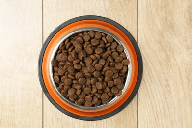 Photo of Dry pet food in feeding bowl on wooden floor, top view