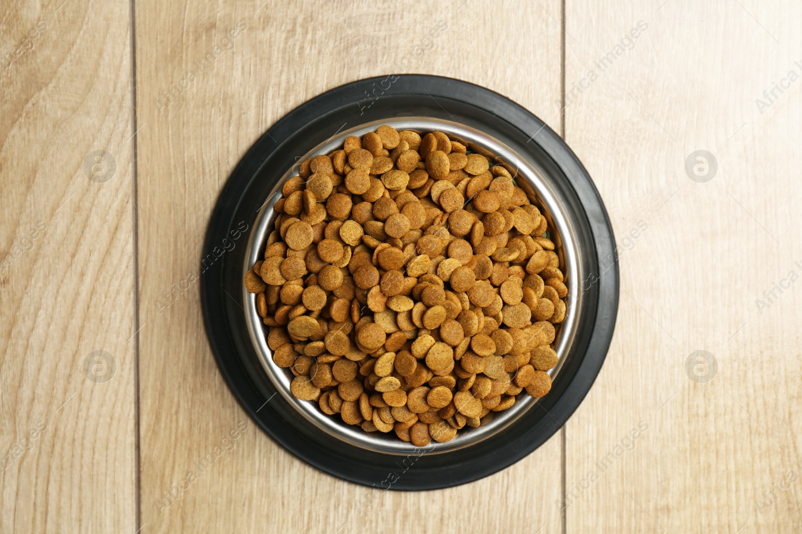 Photo of Dry pet food in feeding bowl on wooden floor, top view