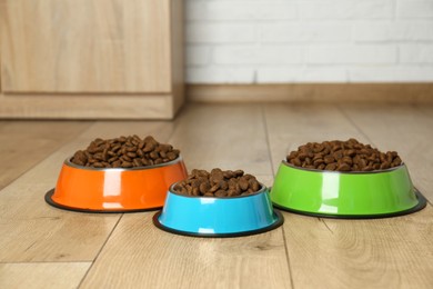 Photo of Dry pet food in feeding bowls on floor indoors