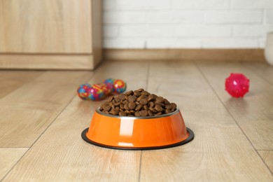 Photo of Dry pet food in feeding bowl and toys on floor indoors