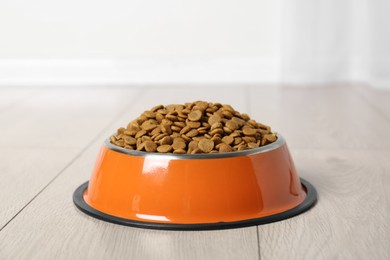 Photo of Dry pet food in feeding bowl on floor indoors, closeup