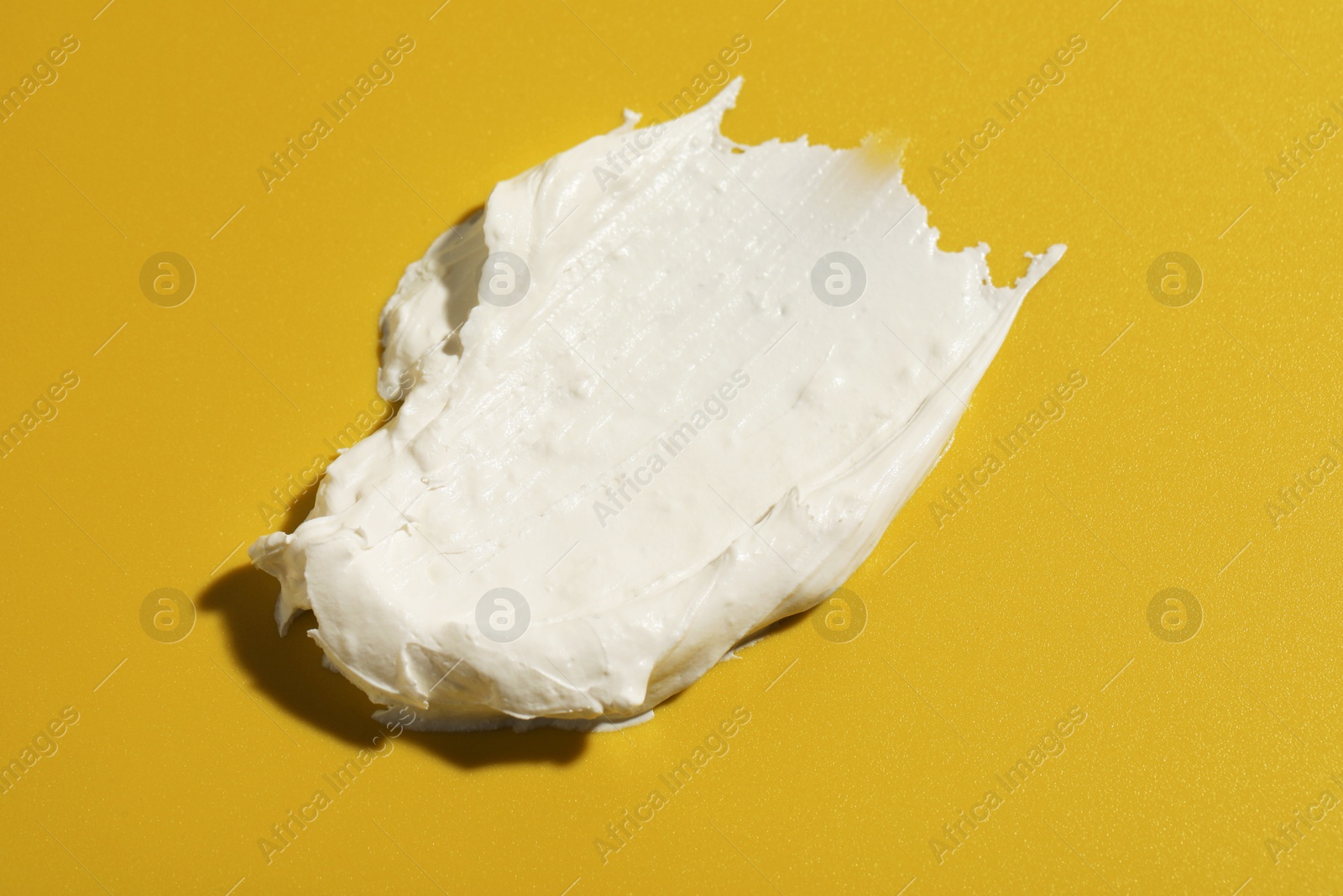 Photo of Cream on dark yellow background, closeup. Sample of cosmetic product