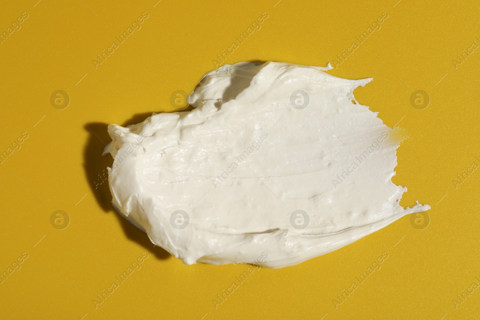 Photo of Cream on dark yellow background, top view. Sample of cosmetic product