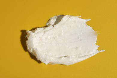 Photo of Cream on dark yellow background, top view. Sample of cosmetic product