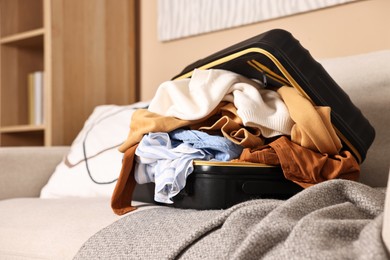 Photo of Open suitcase full of different messy clothes on sofa indoors