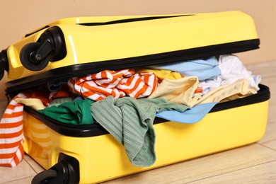 Photo of Open suitcase full of different messy clothes on floor indoors, closeup