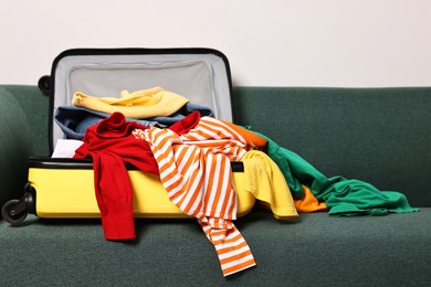 Photo of Open suitcase full of different messy clothes on sofa indoors