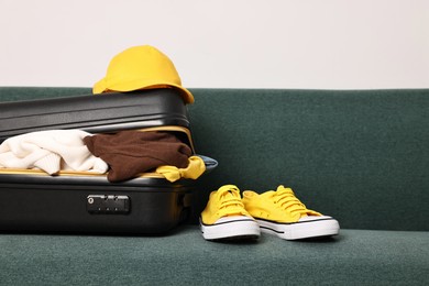 Photo of Open suitcase full of different messy clothes and sneakers on sofa indoors
