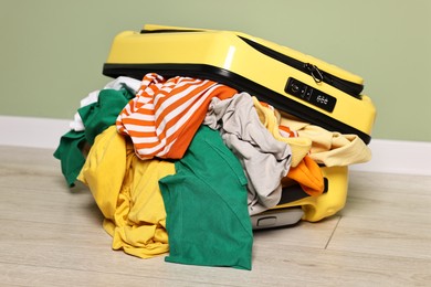 Photo of Open suitcase full of different messy clothes on floor indoors