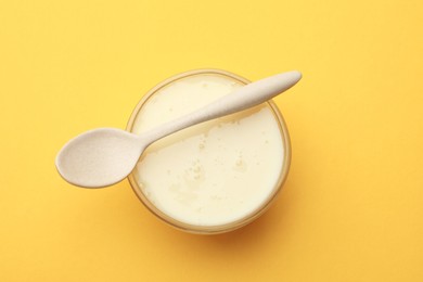 Photo of Tasty condensed milk in bowl and spoon on orange background, top view