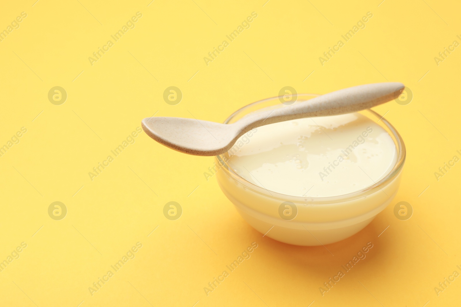 Photo of Tasty condensed milk in bowl and spoon on orange background, closeup. Space for text