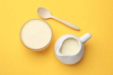 Photo of Tasty condensed milk in bowl and jug with spoon on orange background, top view