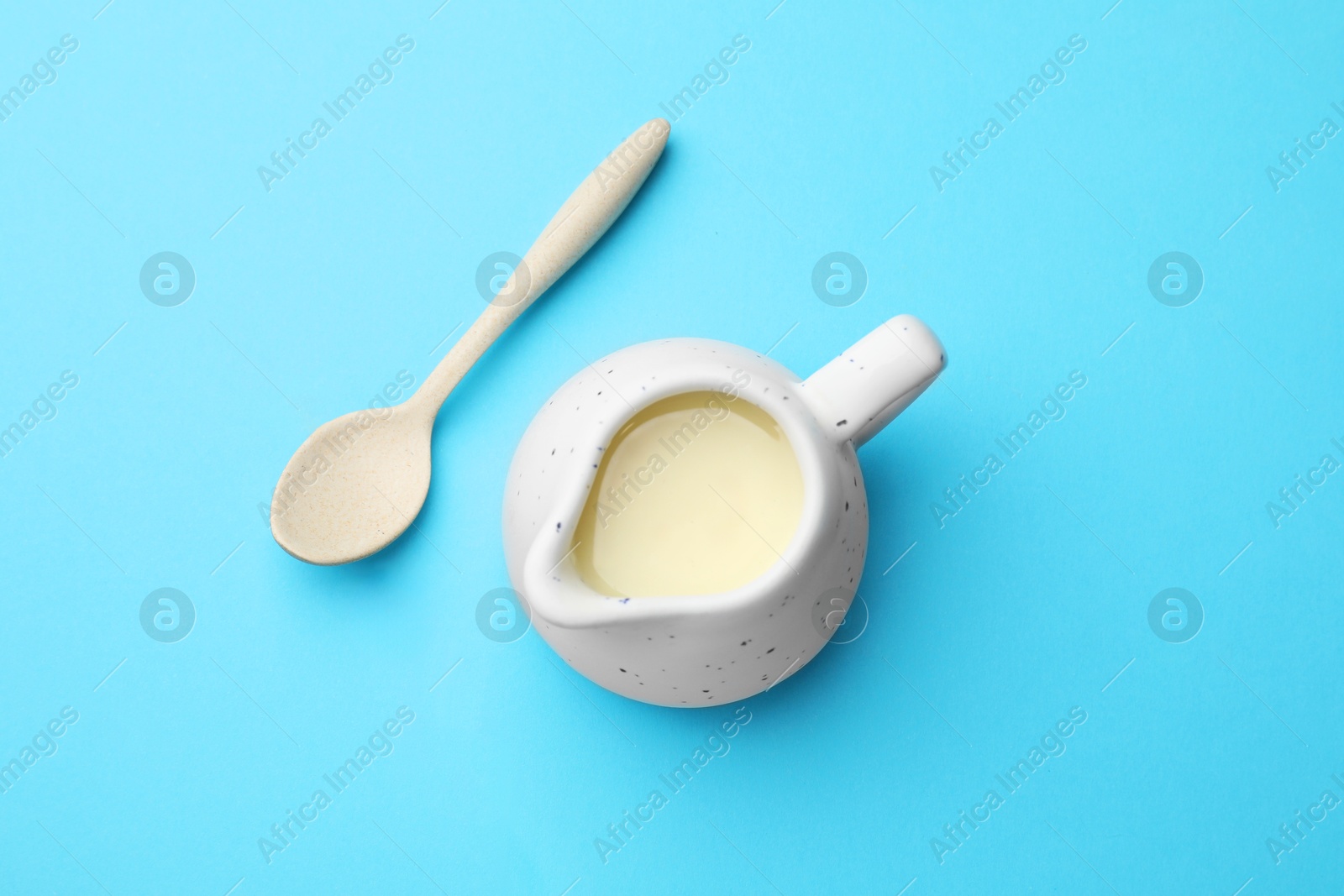 Photo of Tasty condensed milk in jug and spoon on light blue background, top view