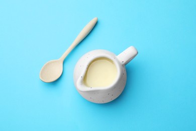 Photo of Tasty condensed milk in jug and spoon on light blue background, top view