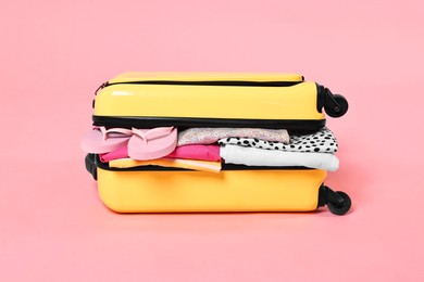 Photo of Packed suitcase full of clothes on pink background