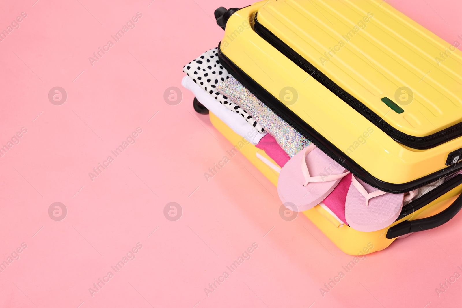 Photo of Packed suitcase full of clothes on pink background, closeup. Space for text
