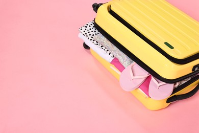 Photo of Packed suitcase full of clothes on pink background, closeup. Space for text
