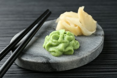 Photo of Marble board with hot wasabi paste, ginger and chopsticks on black textured table, closeup