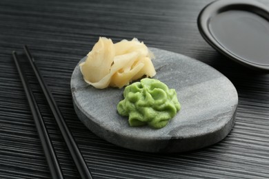 Photo of Hot wasabi paste, soy sauce, ginger and chopsticks on black textured table, closeup