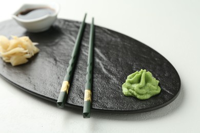 Photo of Hot wasabi paste, soy sauce, ginger and chopsticks on light textured table, closeup