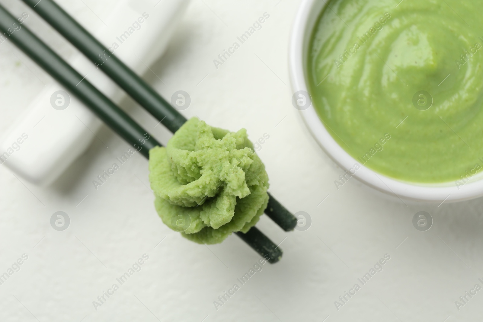 Photo of Chopsticks with hot wasabi paste and bowl on light textured table, flat lay