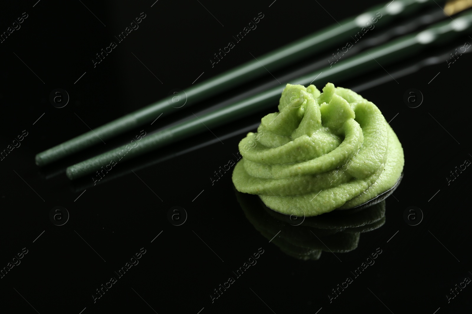 Photo of Hot wasabi paste and chopsticks on black mirror surface, closeup