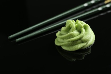 Photo of Hot wasabi paste and chopsticks on black mirror surface, closeup