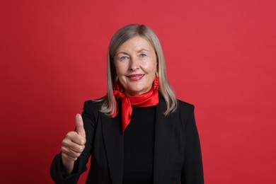 Photo of Senior woman showing thumbs up on red background