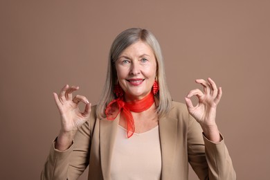 Senior woman showing okay gesture on brown background