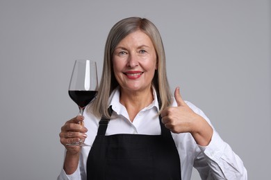 Photo of Senior woman with glass of wine showing thumbs up on grey background