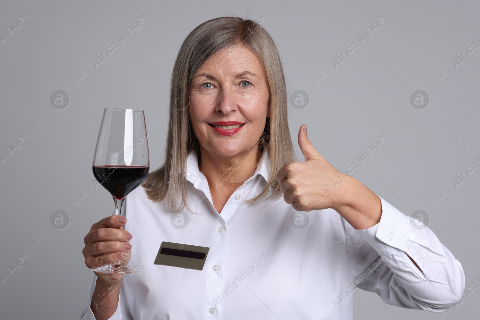 Photo of Senior woman with glass of wine showing thumbs up on grey background