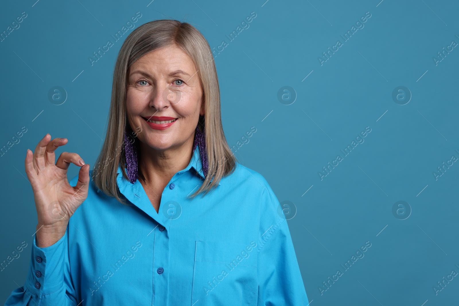 Photo of Senior woman showing okay gesture on blue background. Space for text