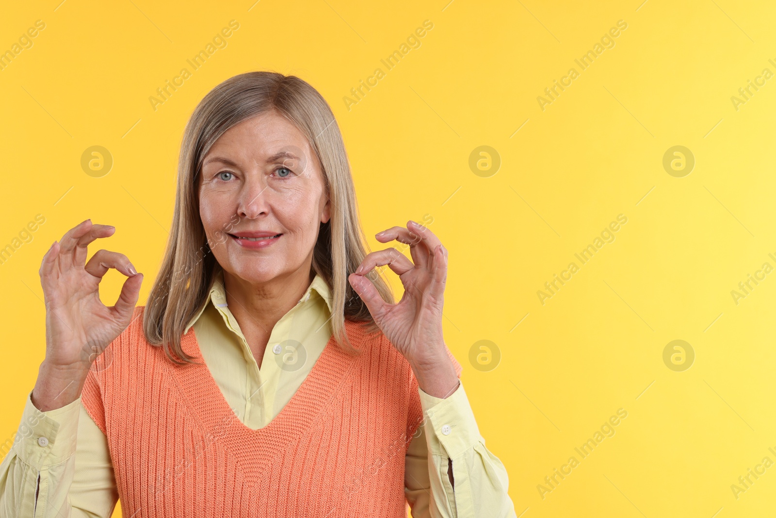 Photo of Senior woman showing okay gesture on yellow background. Space for text