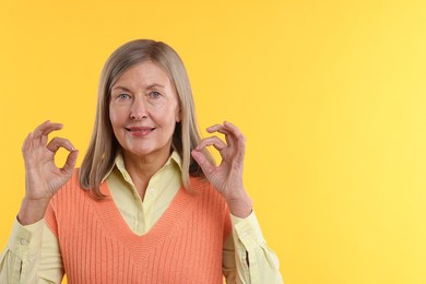 Photo of Senior woman showing okay gesture on yellow background. Space for text