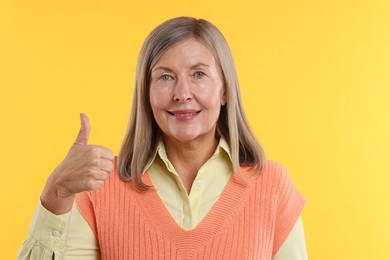 Photo of Senior woman showing thumbs up on yellow background