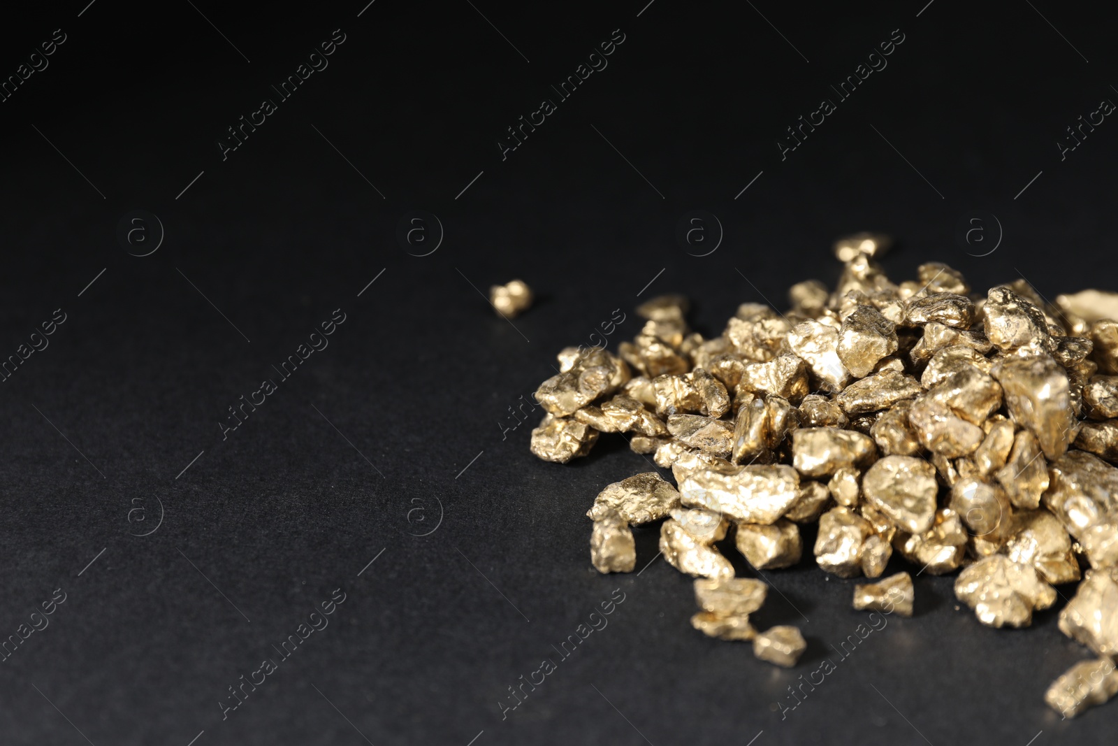 Photo of Shiny gold nuggets on black table, closeup. Space for text