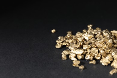 Photo of Shiny gold nuggets on black table, closeup. Space for text