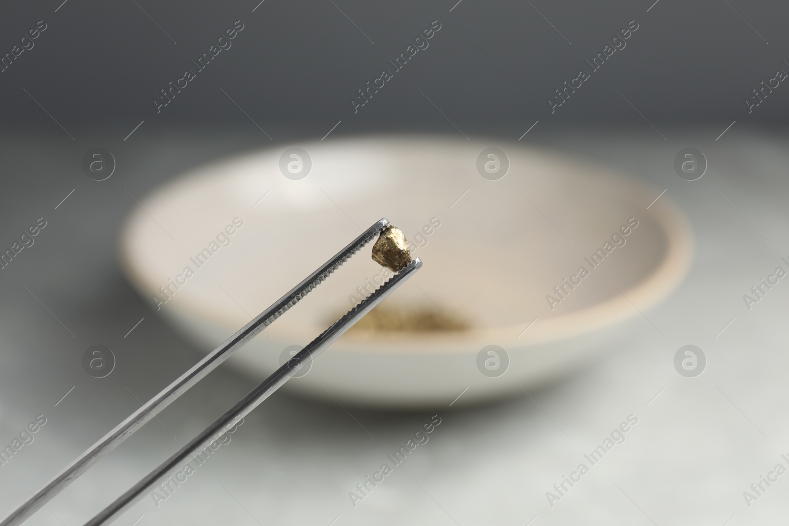 Photo of Tweezers with gold nugget against blurred background, closeup. Space for text