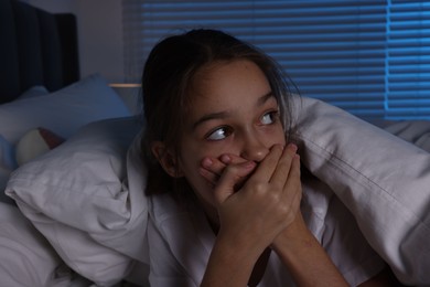 Fearful girl under duvet in bed at night