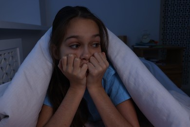 Photo of Afraid girl hiding under duvet on bed at night