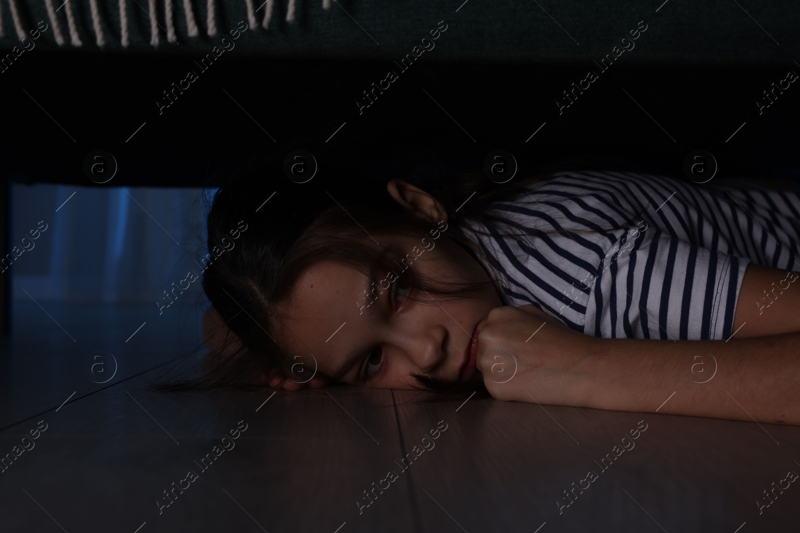 Photo of Fearful girl hiding under bed at night