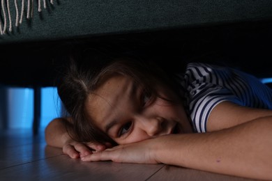 Photo of Fearful girl hiding under bed at night