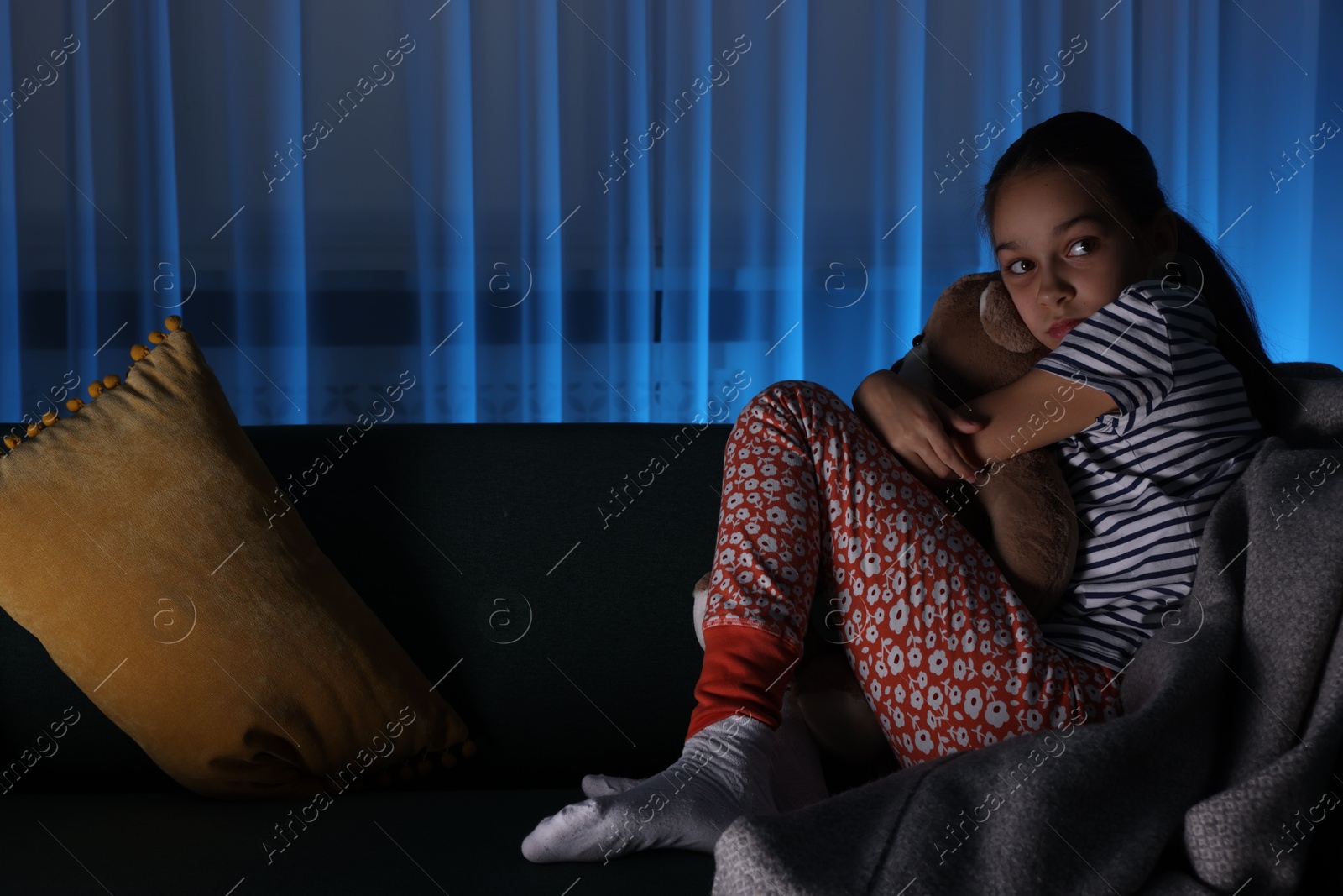 Photo of Afraid girl with teddy bear on sofa at home. Space for text