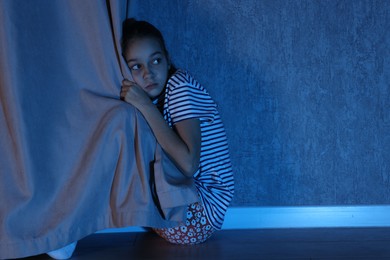 Photo of Scared girl hiding behind curtain at night. Space for text